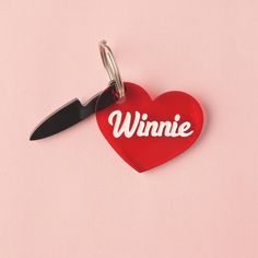 a red heart shaped keychain with the word winnie on it and a knife sticking out of it