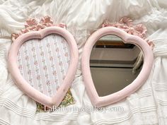 two pink heart shaped mirrors sitting on top of a white bed next to a mirror