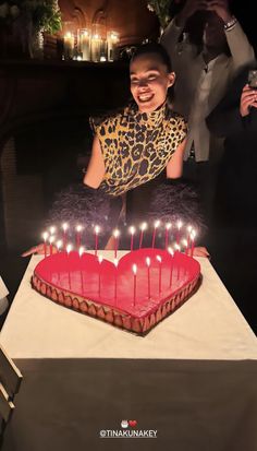 a woman sitting in front of a heart shaped cake with lit candles on the table