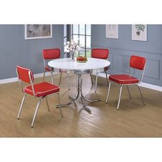 a white table with four red chairs in front of it on a hard wood floor