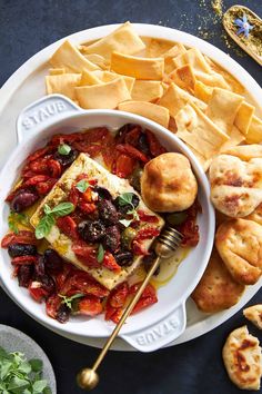 a white bowl filled with lots of food next to crackers and cheese wedges