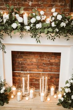 candles are lit in front of a fireplace decorated with greenery and white flowers on the mantle