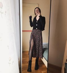 a woman taking a selfie in front of a mirror wearing black boots and a floral print skirt