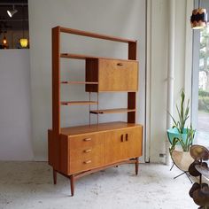 a wooden shelf sitting next to a window in a room with white walls and flooring