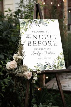 a welcome sign for the night before is decorated with greenery and white roses on an easel