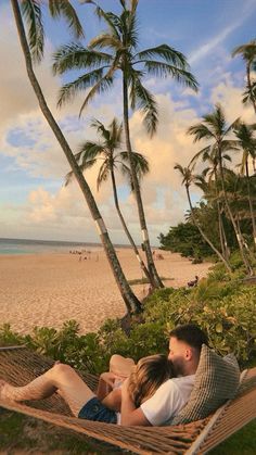 a man and woman laying in a hammock on the beach with palm trees