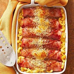 a casserole dish filled with meat and noodles on a wooden table next to a spatula