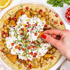 a person is dipping sauce on top of a pita with chickpeas and pomegranates