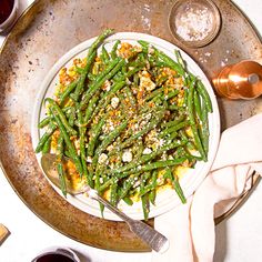 a white plate topped with green beans covered in toppings next to silverware and wine glasses