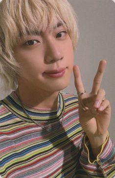 a young man making the peace sign with his hand while wearing a striped shirt and silver ring