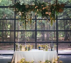 a table with flowers and candles on it in front of a large window that looks out onto the woods