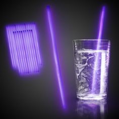 a glass with ice and purple straws next to each other on a black background