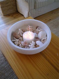 a candle is lit in a bowl filled with seashells on a table next to a couch