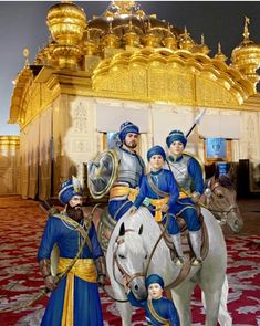 three men in blue and gold outfits riding on a white horse next to a golden building