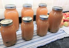 four jars filled with liquid sitting on top of a counter next to apples and other fruit