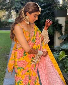 a woman in an orange and pink sari with her hands on her hip, looking down