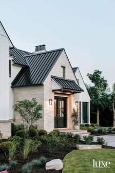 a white house with a black roof and two lights on the front door is surrounded by greenery