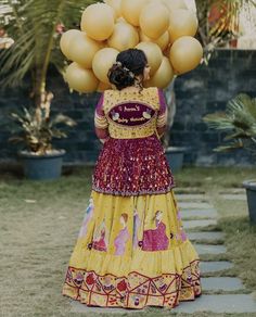 a woman in a yellow and red dress carrying balloons on her head