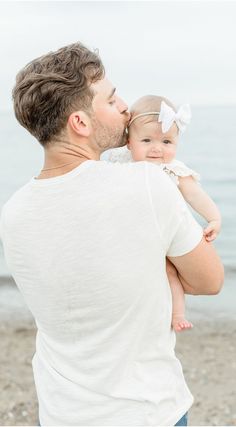 a man holding a baby in his arms on the beach while looking at the water