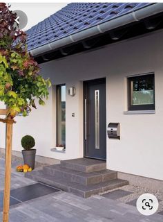 a white house with a black door and some plants on the side of the building