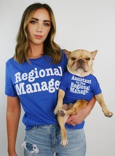 a woman holding a small dog wearing a shirt that says regional manager on it's chest