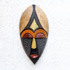 Add a touch of royalty to your home with this African mask from Ghana. By Victor Dushie this mask is hand-carved from sese wood. Two beige sections accentuate the top of the head while the eyes lips and brow are painted red and yellow. Embossed brass and aluminum further decorate this beautiful mask. Coconut Ideas, Afro Ideas, Cardboard Mask, Wood Mask, Mask Wall, Wall Mask, African Mask, Beautiful Mask, African Masks