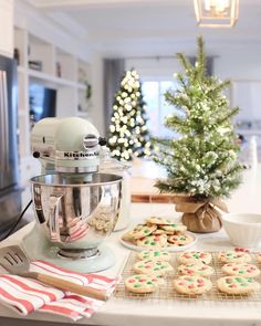 a kitchen counter topped with cookies next to a mixer and christmas tree in the background