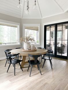 a dining room table with black chairs and a white vase filled with flowers on top