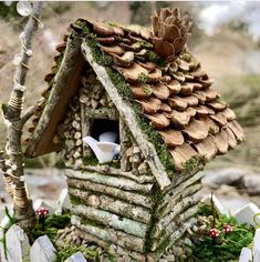 a bird house made out of logs and rocks with a roof that is covered in moss