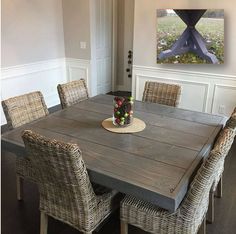 a dining room table with wicker chairs and a painting on the wall behind it