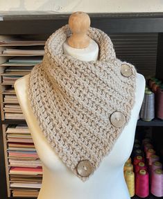 a white mannequin wearing a beige knitted cowl with buttons on it