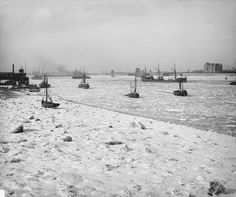 black and white photograph of boats in the water on ice covered beach with buildings in background