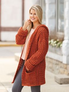 a woman wearing an orange cardigan and black leggings standing on the sidewalk