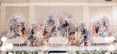 an elaborately decorated stage with white couches and flowers on the wall behind it