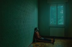 a woman sitting on the floor in an empty room with green light coming from a window