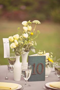 the table is set with white and yellow flowers in vases, wine glasses, and napkins