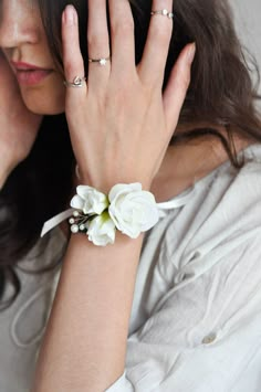 a woman with her hand on her face wearing a white flower bracelet and matching rings