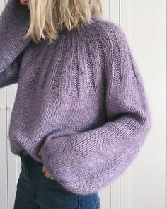 a woman wearing a purple sweater is standing in front of a white wall and has her hands on her head