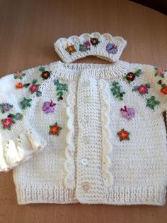 a white knitted sweater with flowers on the collar and sleeves is sitting on a table