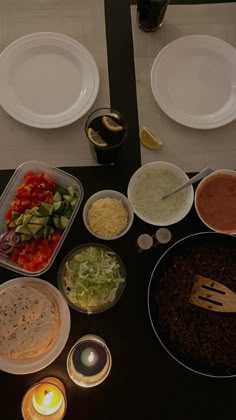 a table topped with plates and bowls filled with different types of food next to candles