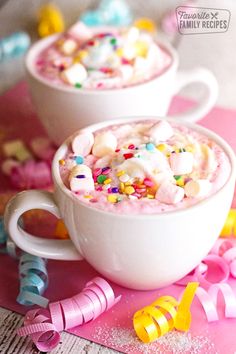 two cups filled with marshmallows and sprinkles on top of pink paper