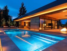 an outdoor swimming pool at night with lights on the side and fire pit in the middle