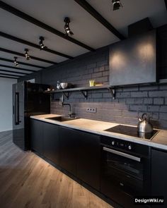 an empty kitchen with black cabinets and wood flooring on the walls is lit by recessed lighting