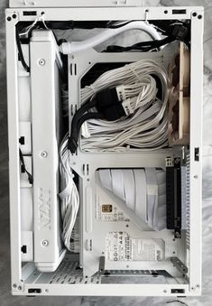 the inside of a white computer case with wires and other items in it on a marble surface