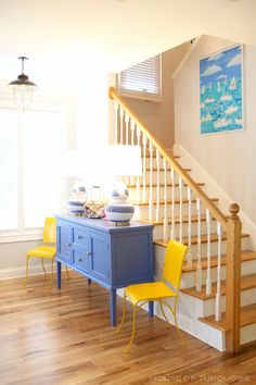 two yellow chairs are sitting in front of a blue dresser and stairs that lead up to the second floor