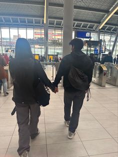 two people holding hands while walking through an airport with luggage bags on their back and in front of them