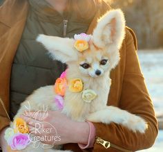 a woman is holding a small dog with flowers on it's head and wearing a jacket