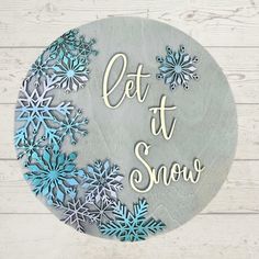 a sign that says let it snow on the side of a wooden wall with blue and white snowflakes