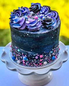 there is a blue cake with purple flowers on the top and sprinkles all over it