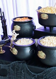 three black caulders filled with popcorn sitting on top of a purple table cloth